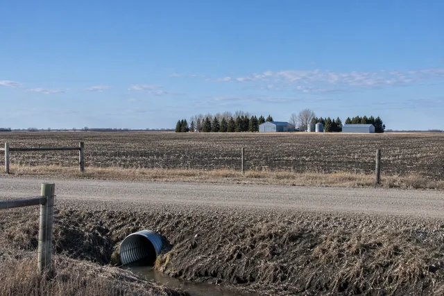 Rural property boundary with a gravel section road, deep ditches and a farmstead set back behind its shelterbelt
