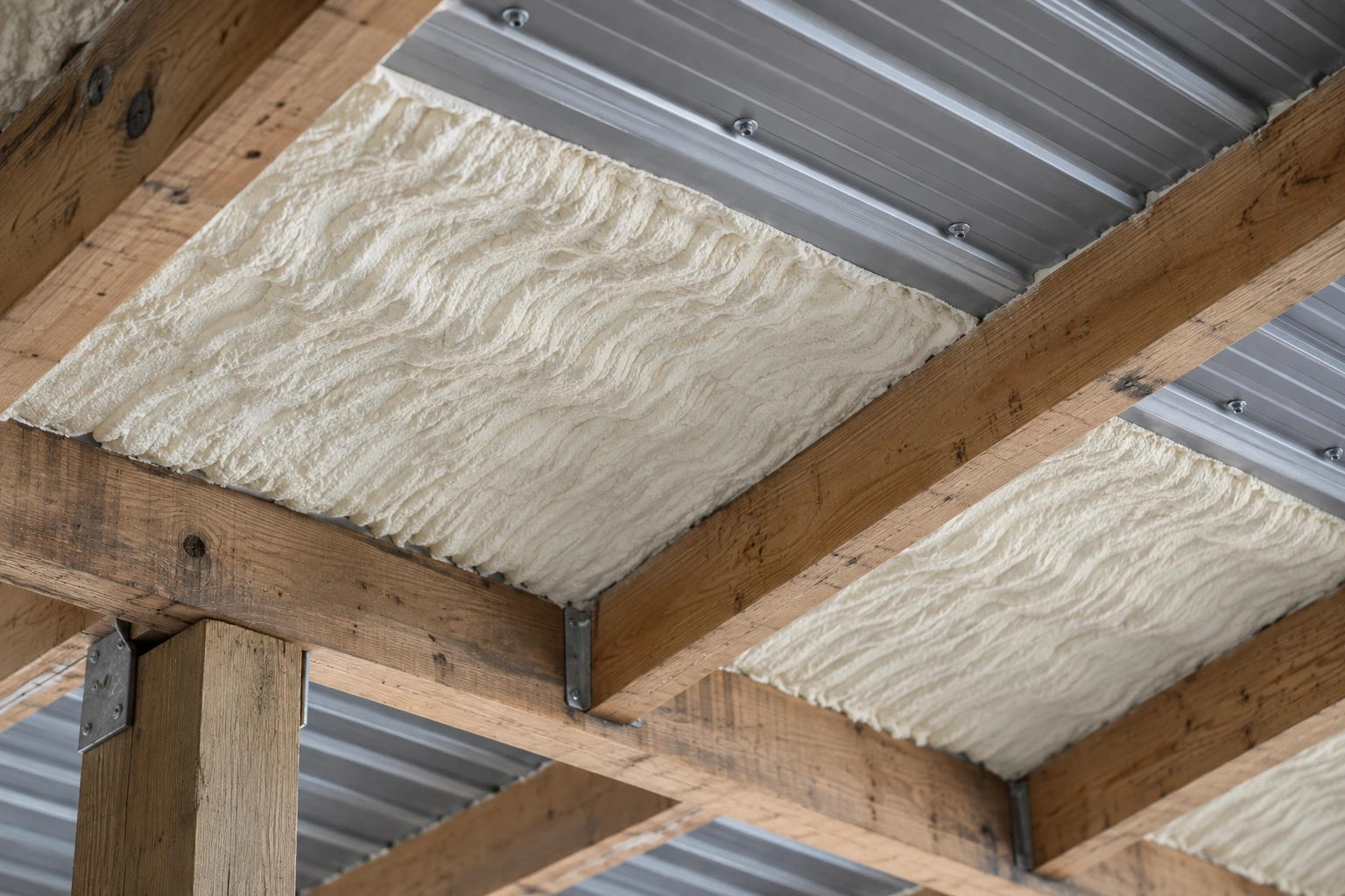 Post-frame wall part insulated with batt between girts and a poly vapour retarder stapled over the finished section